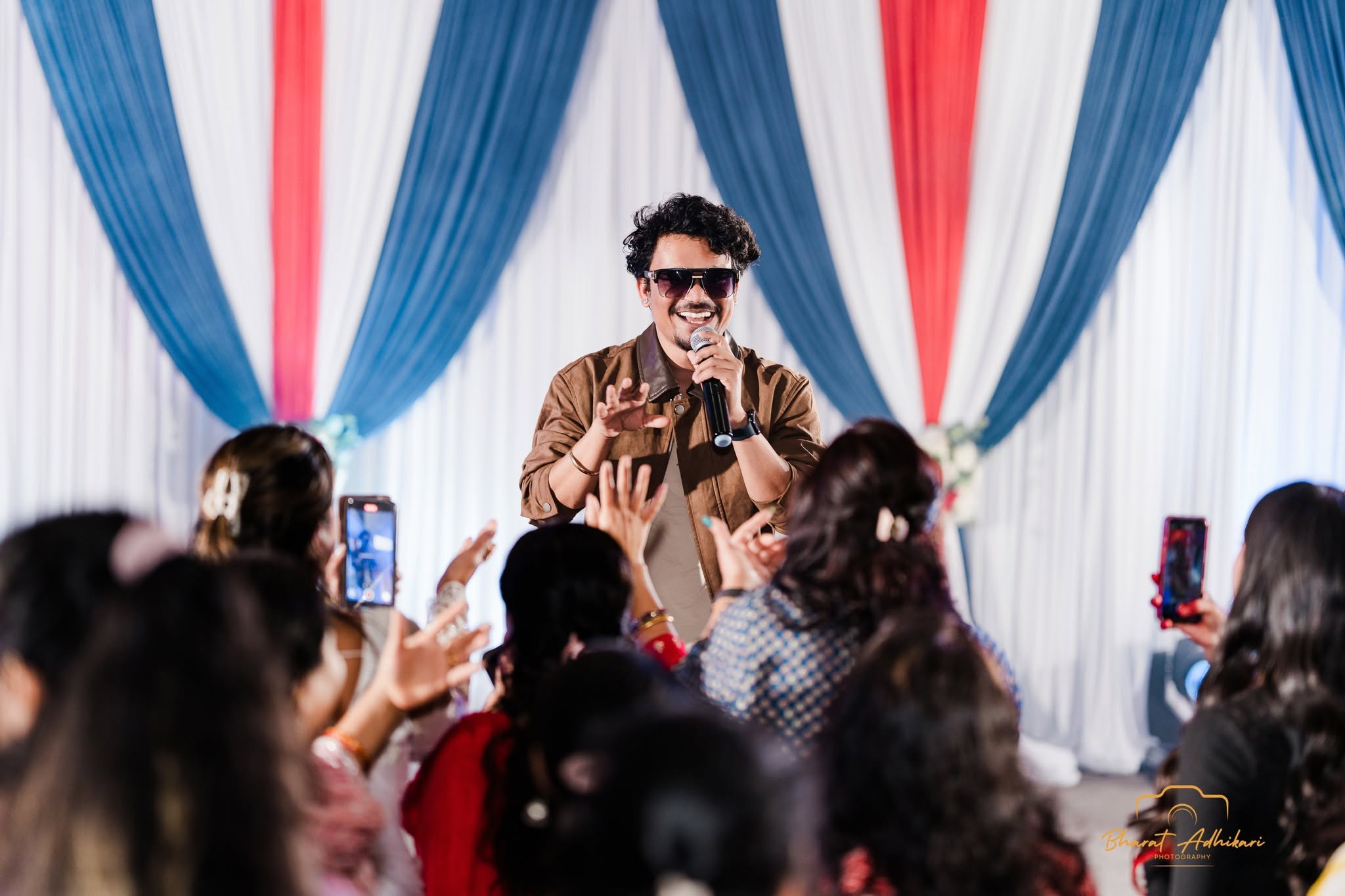 A singer performing live on stage as the crowd raises their hands